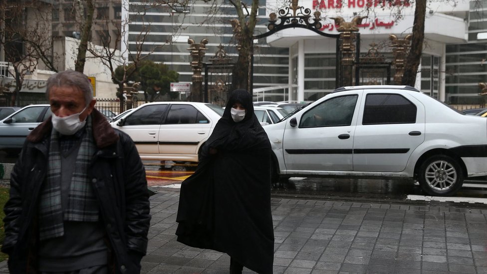 رجل وامرأة يرتديان كمامة خوفا من الإصابة بالفيروس أمام مستشفى في إيران