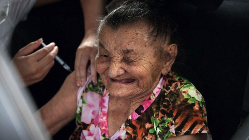 امرأة برازيلية مسنة تتلقى جرعة من لقاح كورونافاك في رحلة بالسيارة من خلال مركز التطعيم في ريو دي جانيرو ، البرازيل، في 6 فبراير/شباط 2021.