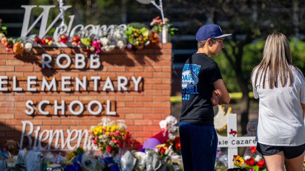 شباب بالغون ينظرون إلى نصب تذكاري في مدرسة روب الابتدائية بعد إطلاق نار جماعي في 26 مايو/ أيار 2022 في أوفالدي، تكساس.
