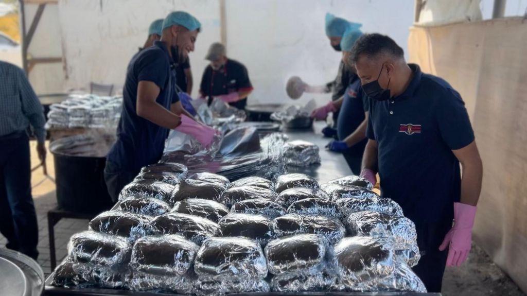 رجال يقفون أمام أطعمة مغلفة في أحد المطابخ العامة