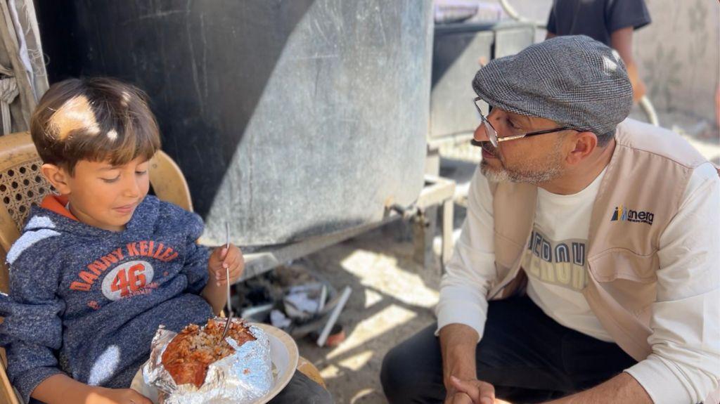 سامي مطر مع أحد أطفال المخيم الذي يتناول وجبة من الطعام