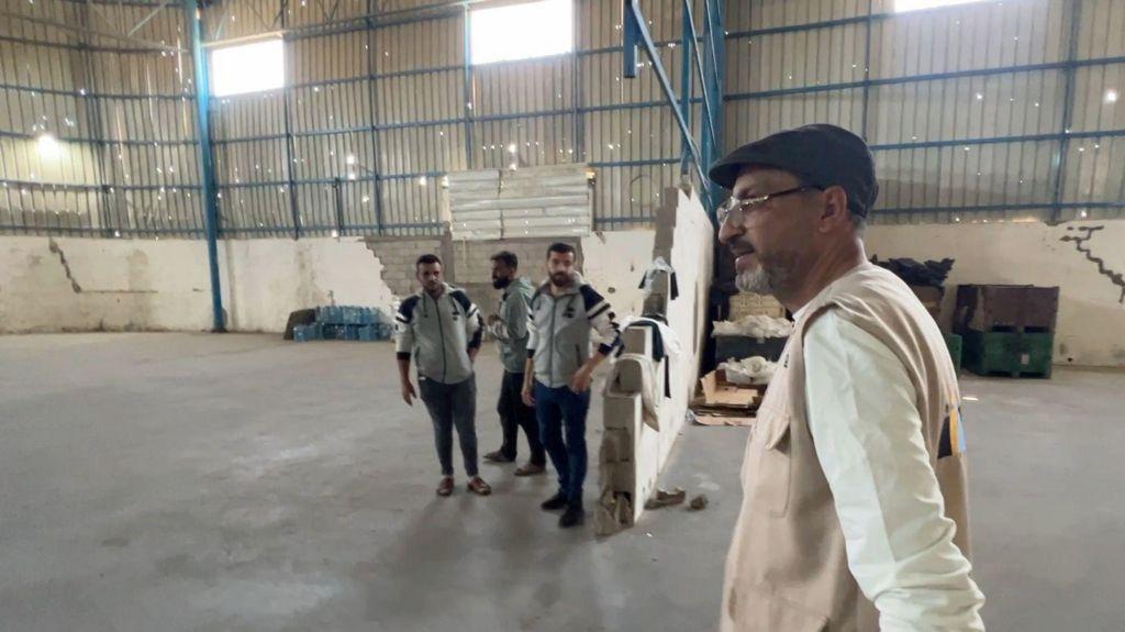 سامي مطر يصطحب صحفياً محلياً من بي بي سي في جولة في مستودع (أنيرا) الفارغ.